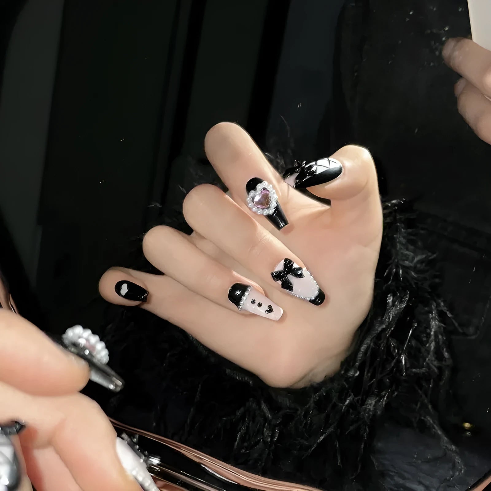 Black plastic false nails with hand-painted pink hearts, bow, and XINGX patterns in cat's eye style.
