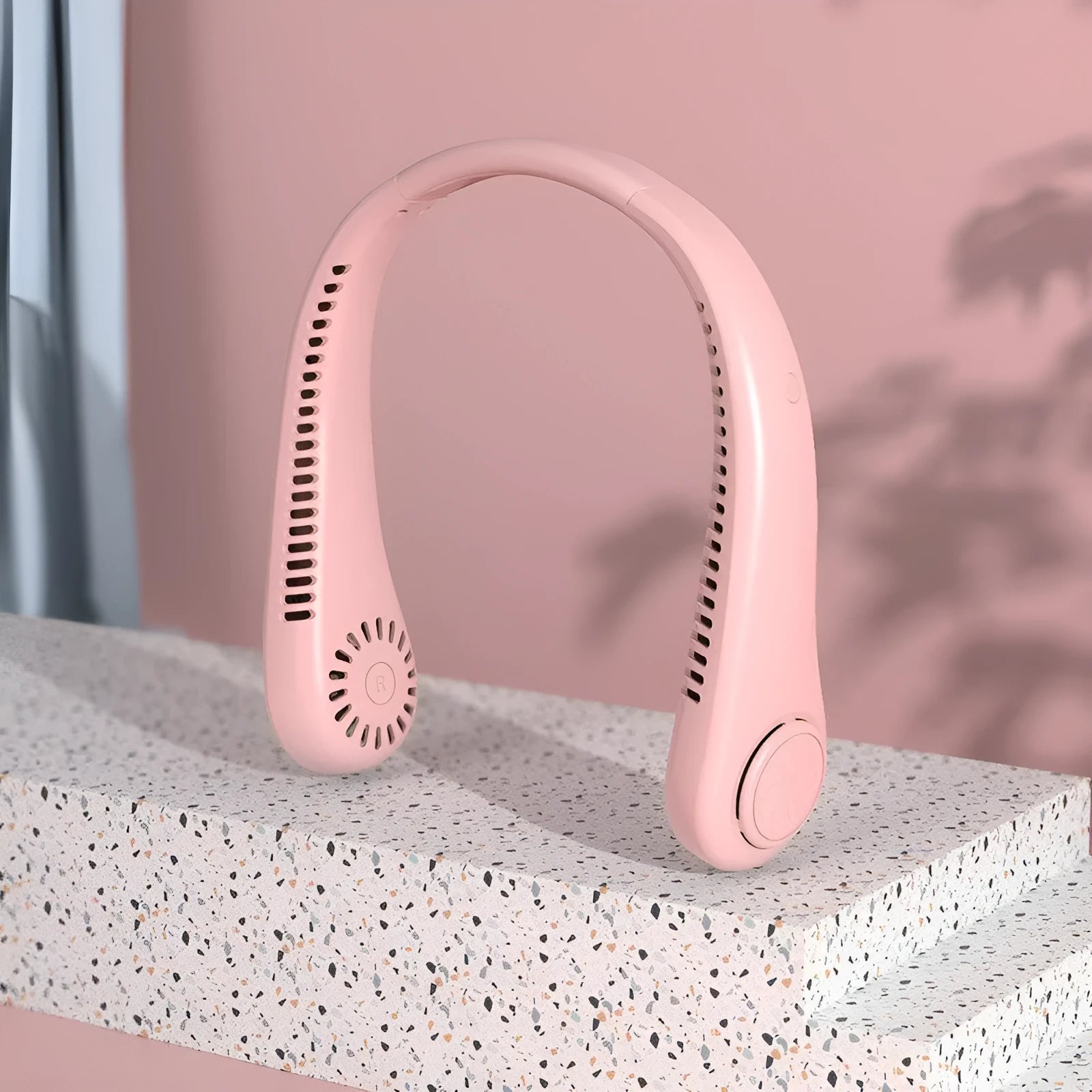Pink bladeless neck fan hanging with USB cable for charging.
