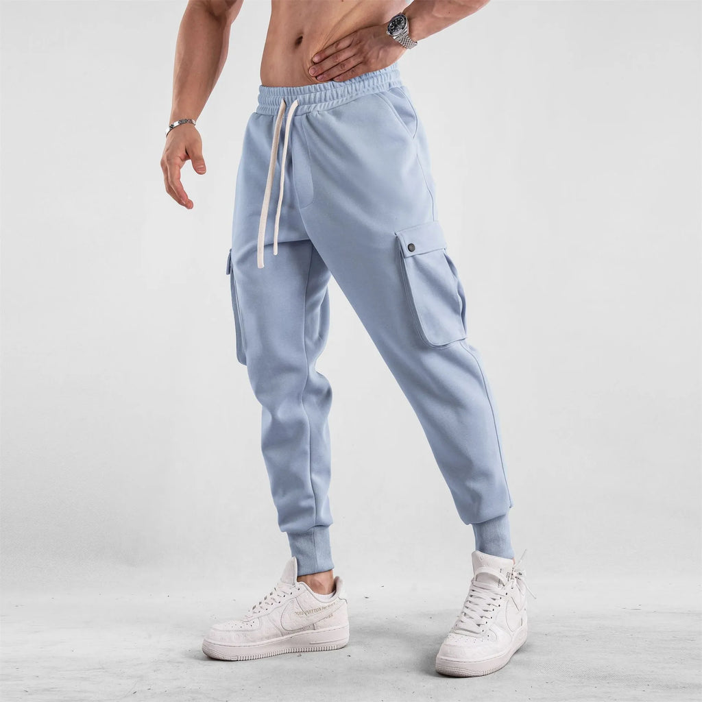 Man wearing loose fit apricot coloured cotton sports trousers with ankle ties and multiple pockets.