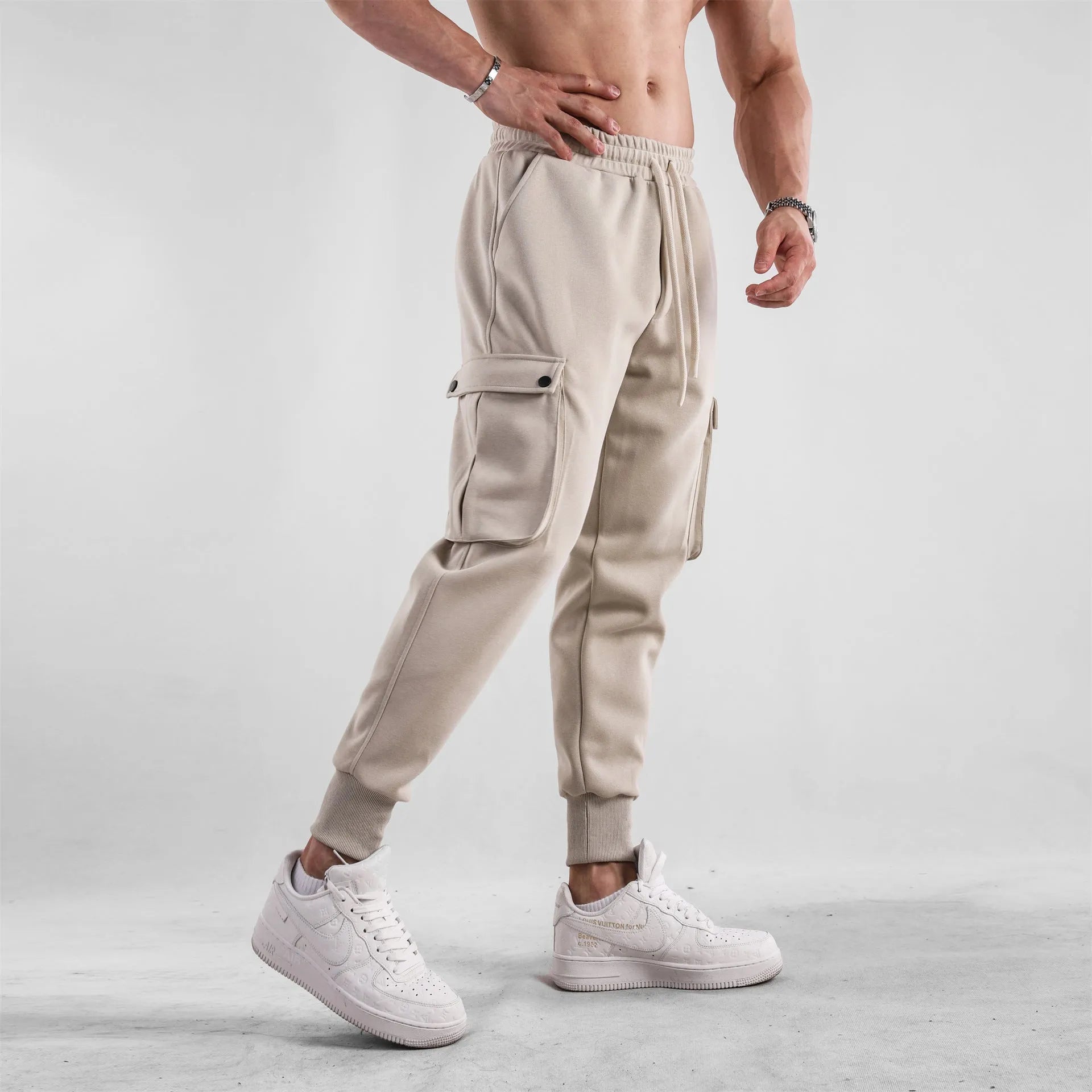 Man wearing loose fit apricot coloured cotton sports trousers with ankle ties and multiple pockets.