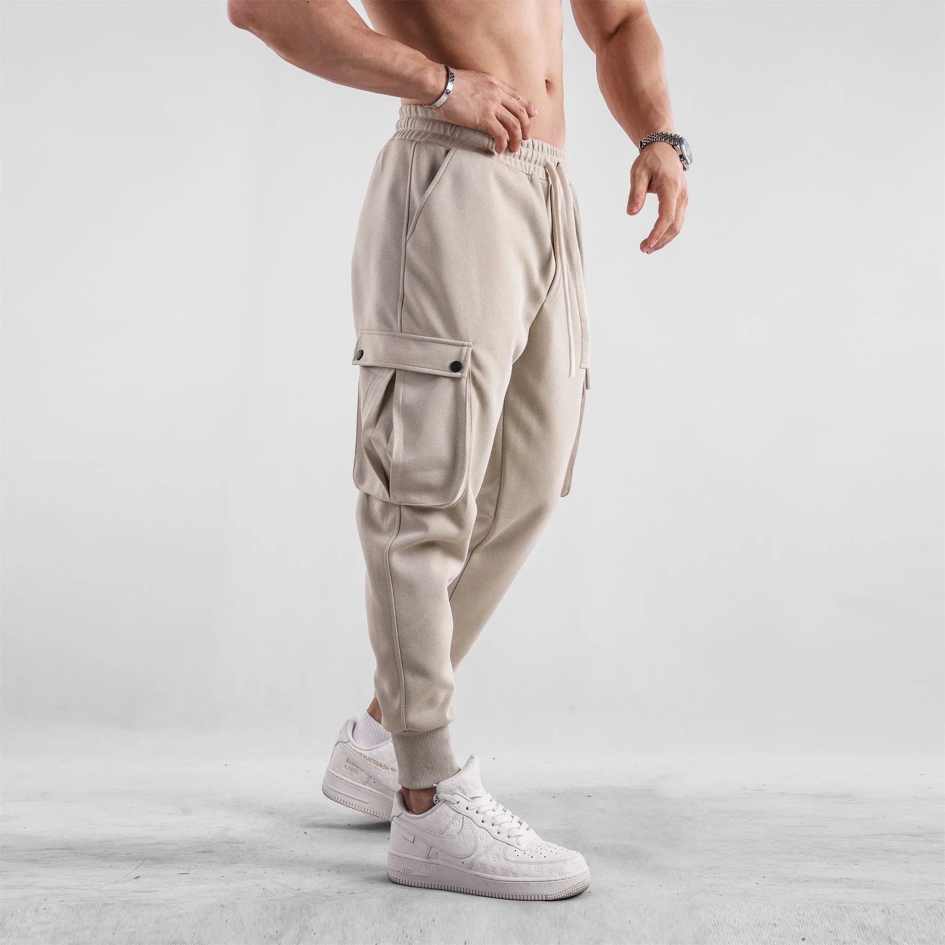 Man wearing loose fit apricot coloured cotton sports trousers with ankle ties and multiple pockets.