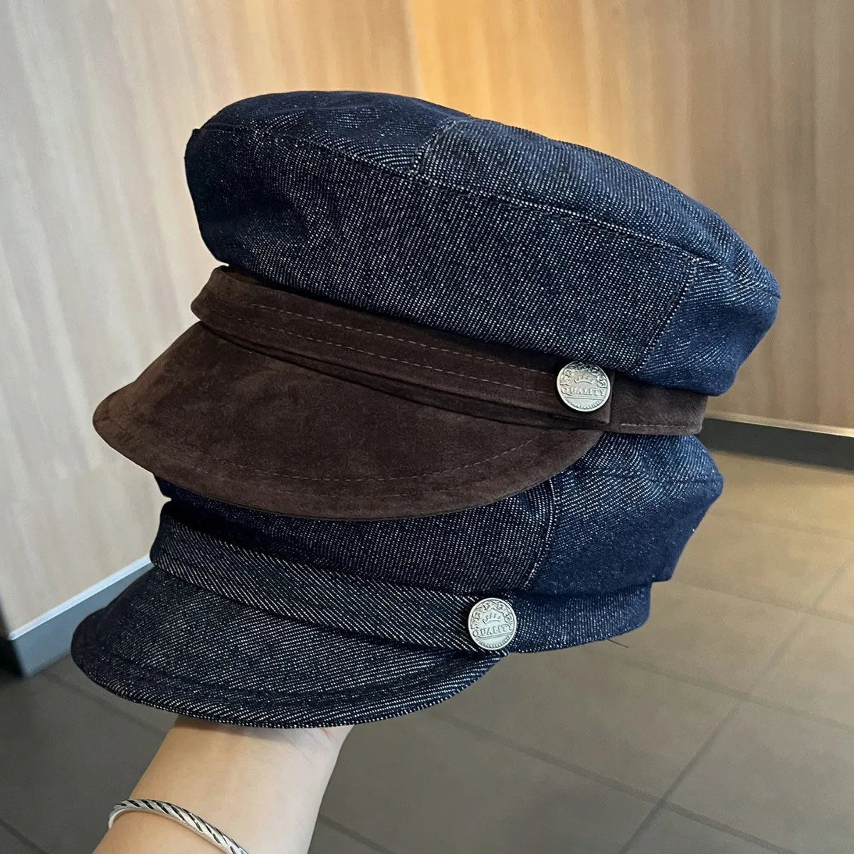 Dark blue denim newsboy cap with an adjustable strap and octagonal shape on a neutral background.