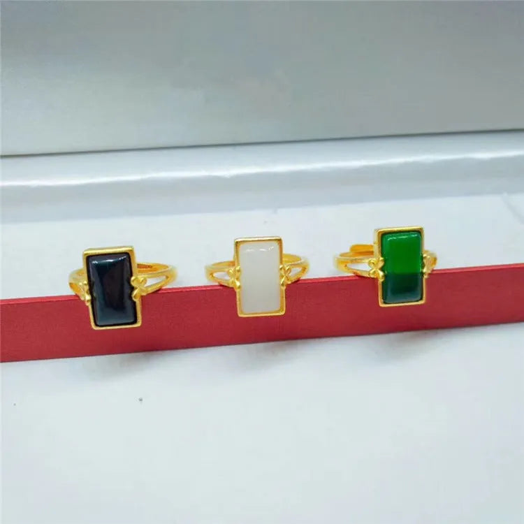 Adjustable gold-coloured brass ring with a large inlaid gemstone, shown in green, white, and black colour options.