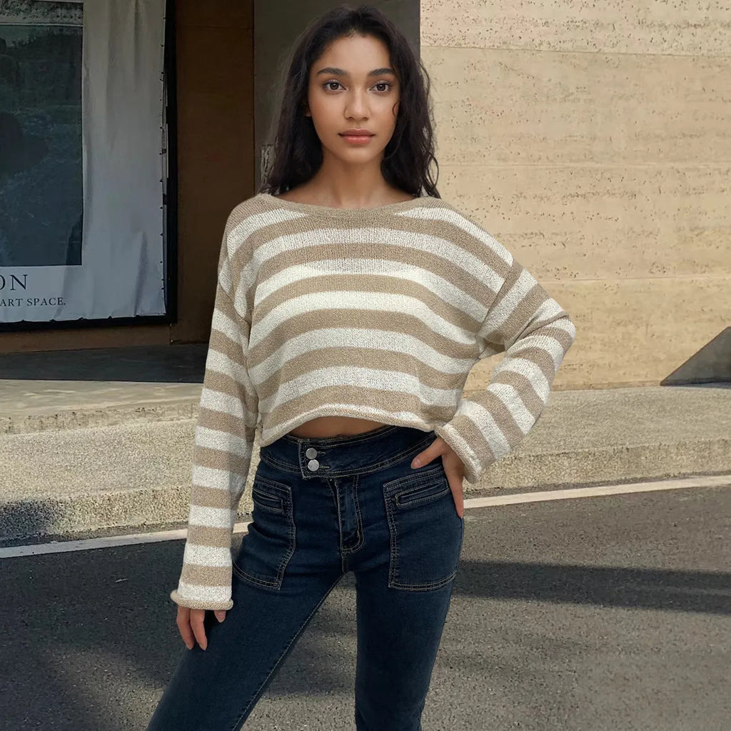 A woman wearing a black and white striped, cropped, long-sleeved sweater, showing the front and back reversible design.