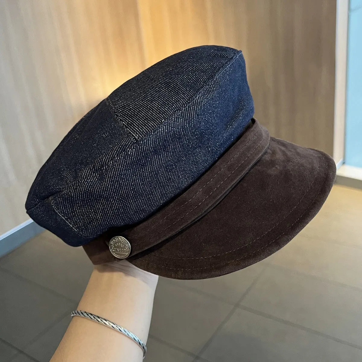 Dark blue denim newsboy cap with an adjustable strap and octagonal shape on a neutral background.