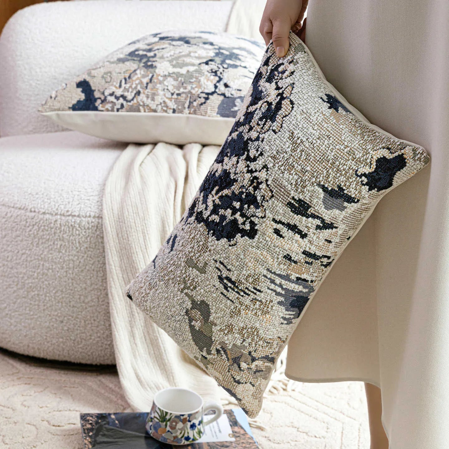 Antique blue abstract floral decorative pillow on a grey sofa, showing square and waist pillow sizes.