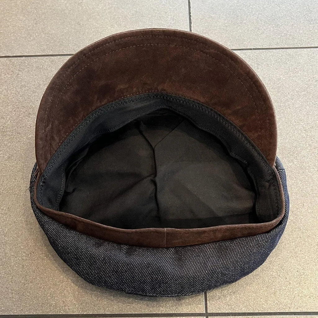 Dark blue denim newsboy cap with an adjustable strap and octagonal shape on a neutral background.