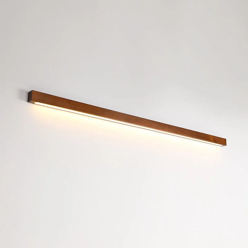 A long, slim walnut-coloured wooden and acrylic LED strip light mounted on a wall.