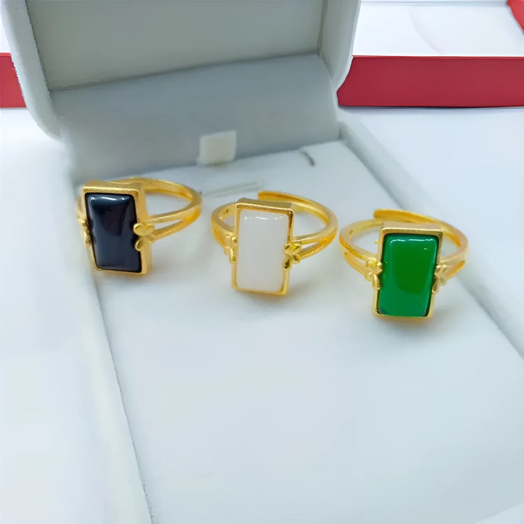 Adjustable gold-coloured brass ring with a large inlaid gemstone, shown in green, white, and black colour options.