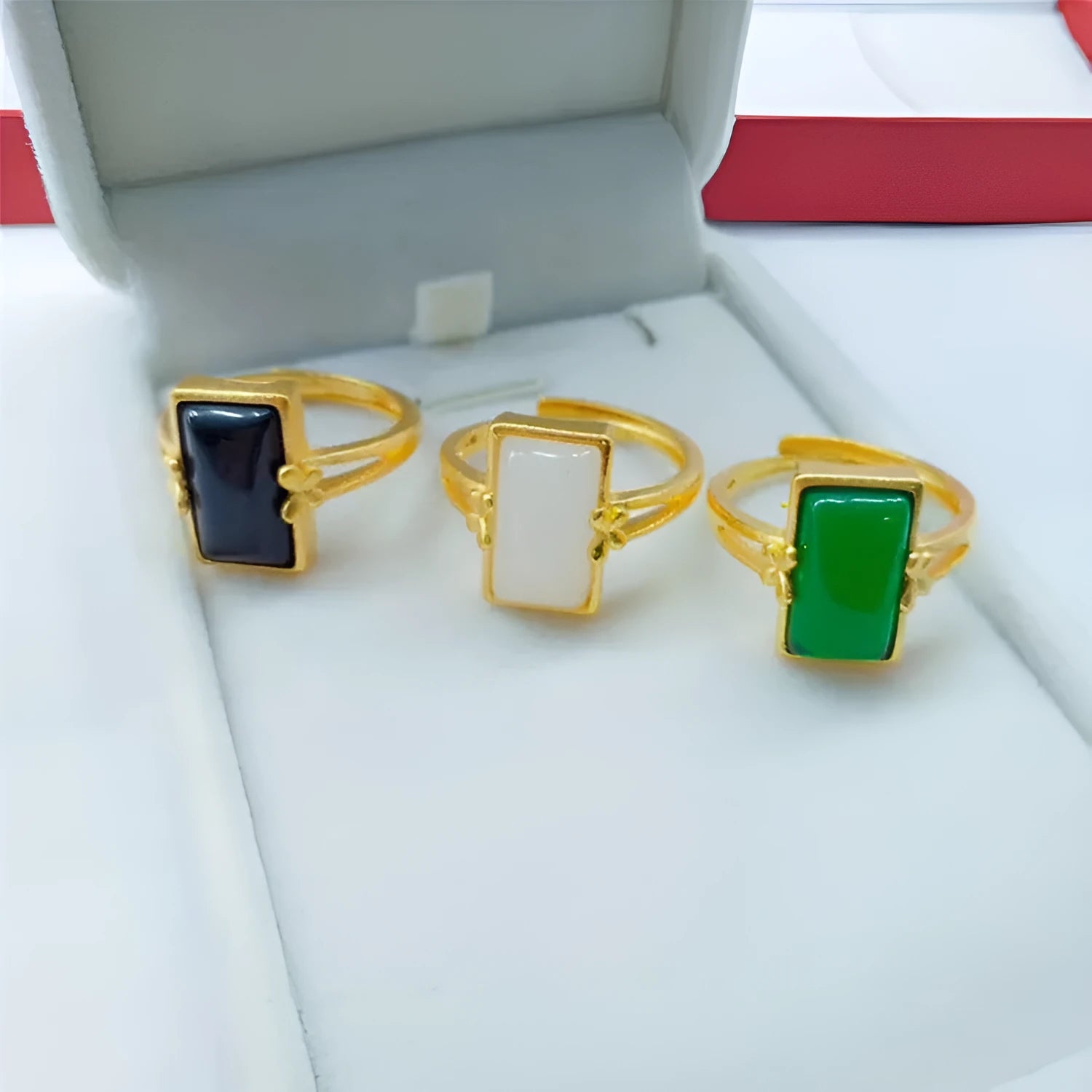 Adjustable gold-coloured brass ring with a large inlaid gemstone, shown in green, white, and black colour options.