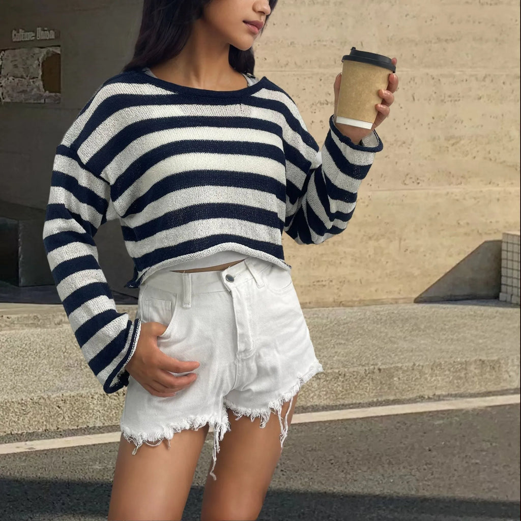 A woman wearing a black and white striped, cropped, long-sleeved sweater, showing the front and back reversible design.