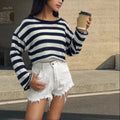 A woman wearing a black and white striped, cropped, long-sleeved sweater, showing the front and back reversible design.