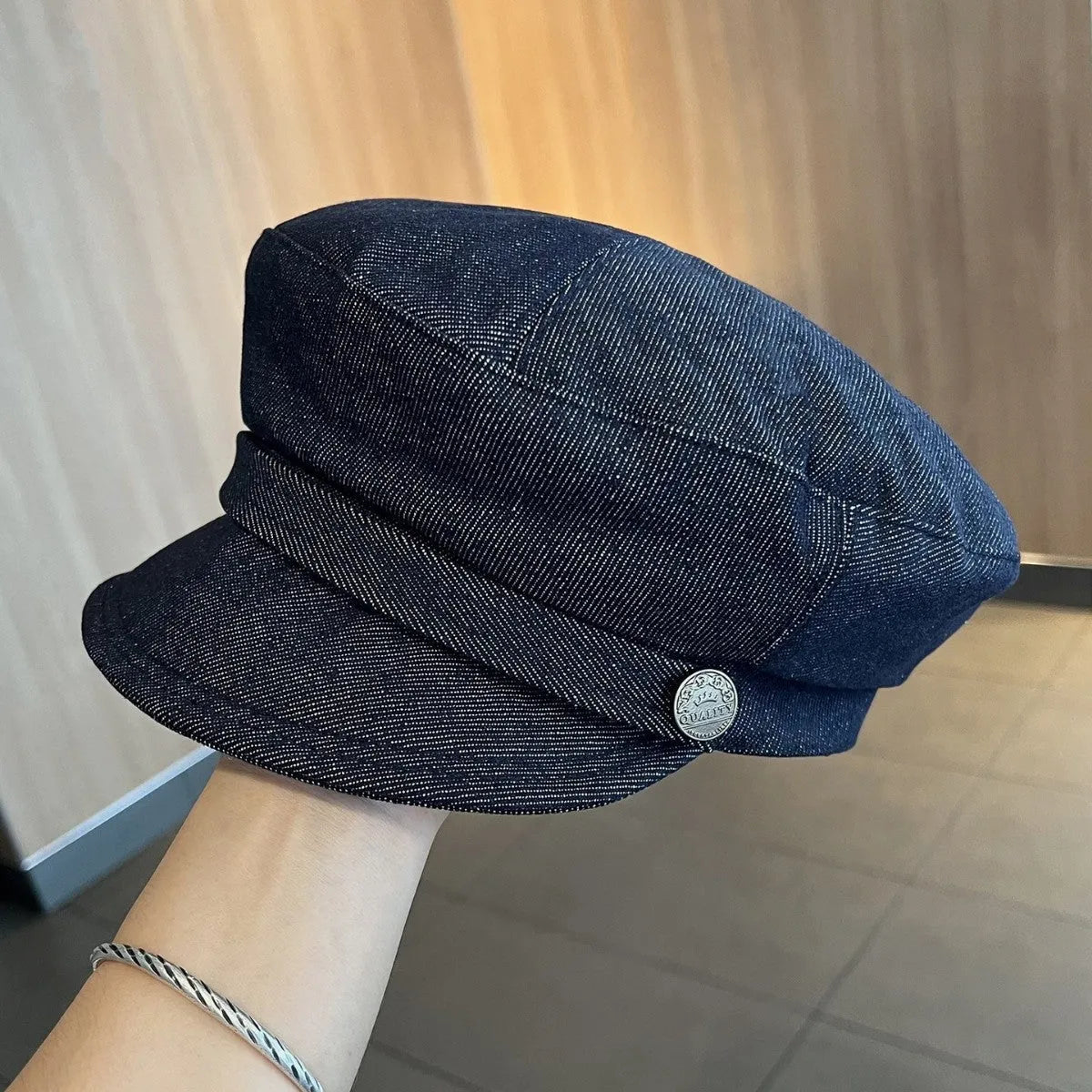 Dark blue denim newsboy cap with an adjustable strap and octagonal shape on a neutral background.