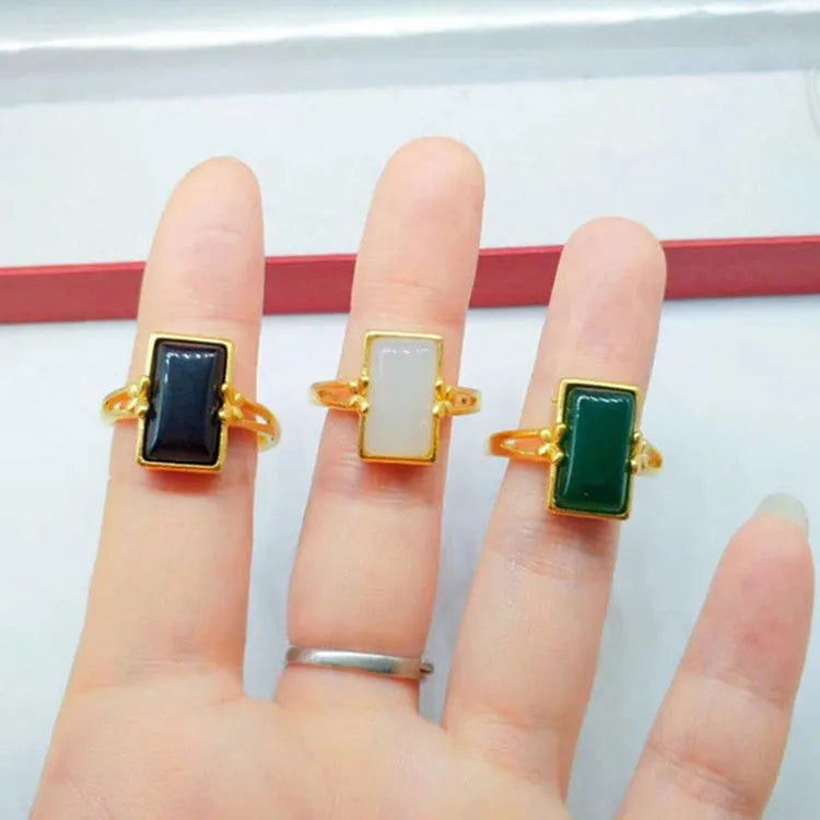 Adjustable gold-coloured brass ring with a large inlaid gemstone, shown in green, white, and black colour options.