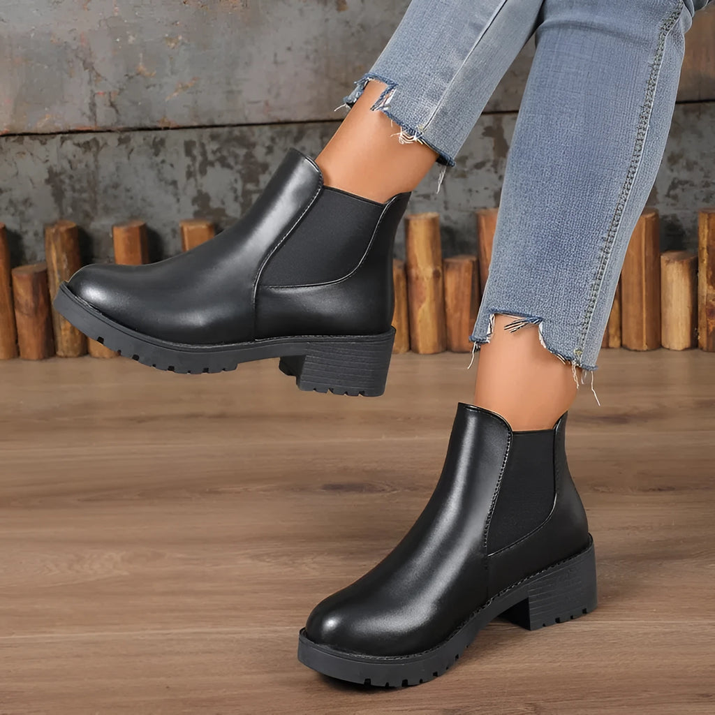 Black Chelsea ankle boots for women with flat chunky heel, round toe, and cloth upper on a light background