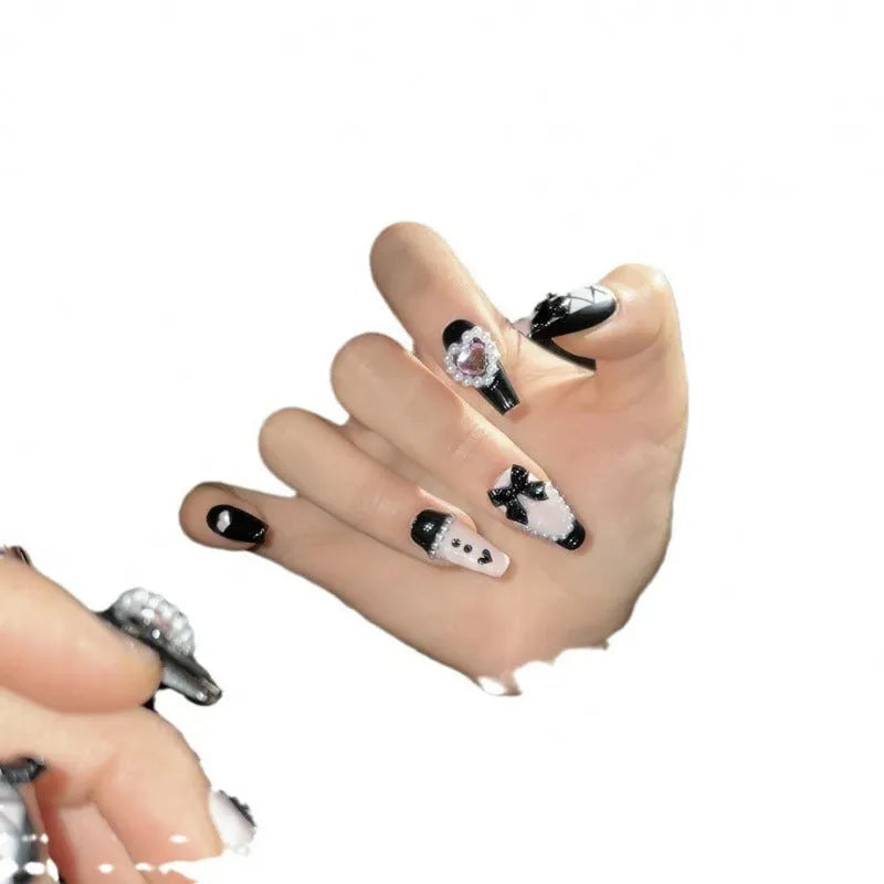 Black plastic false nails with hand-painted pink hearts, bow, and XINGX patterns in cat's eye style.