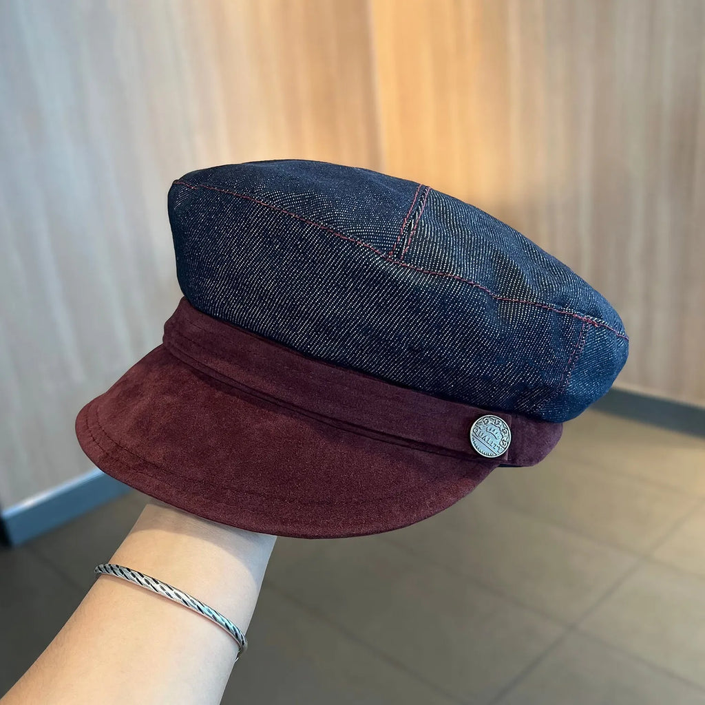 Dark blue denim newsboy cap with an adjustable strap and octagonal shape on a neutral background.