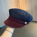 Dark blue denim newsboy cap with an adjustable strap and octagonal shape on a neutral background.