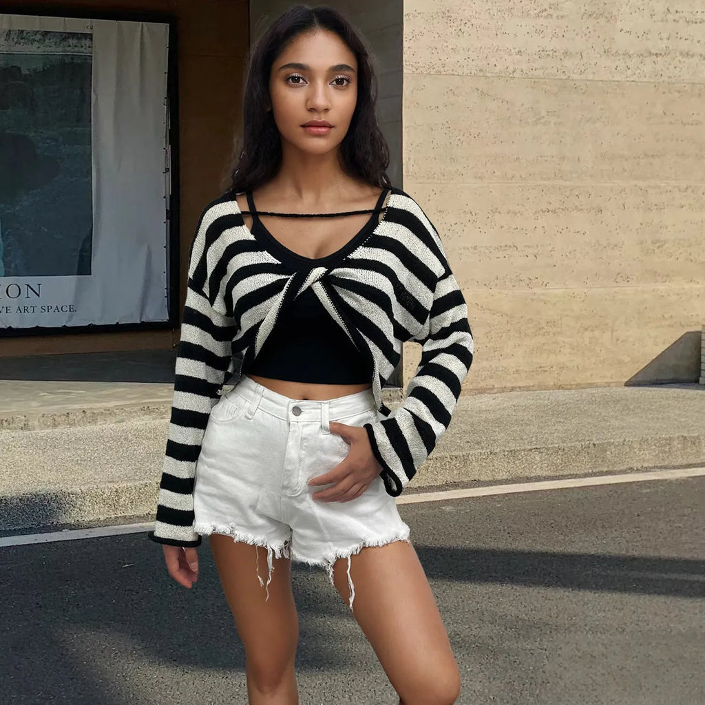 A woman wearing a black and white striped, cropped, long-sleeved sweater, showing the front and back reversible design.