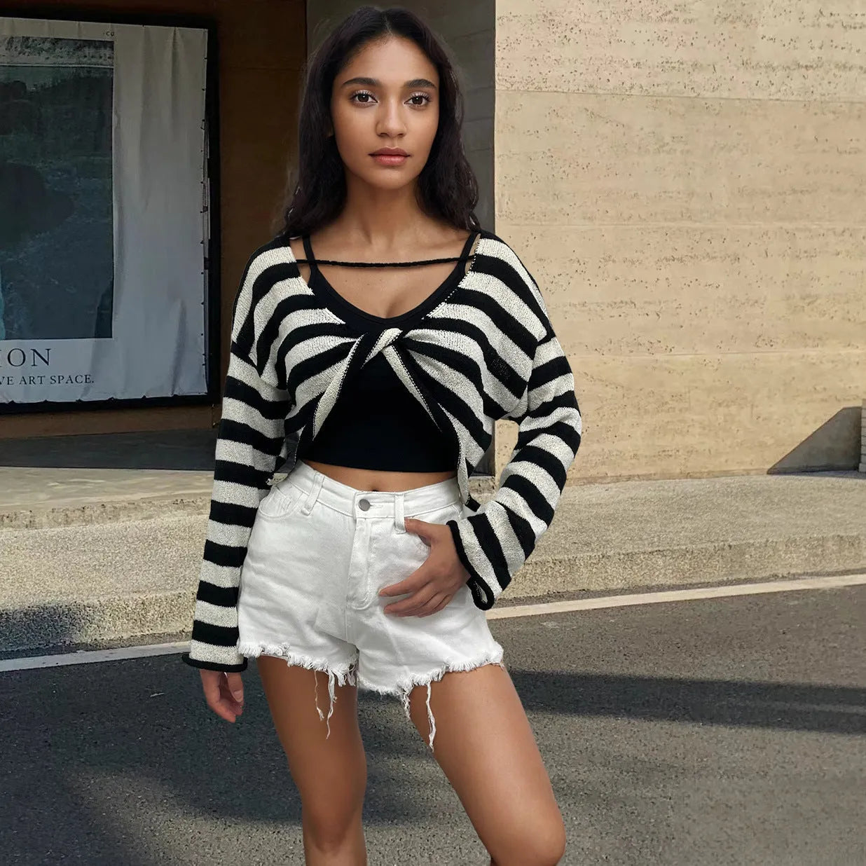 A woman wearing a black and white striped, cropped, long-sleeved sweater, showing the front and back reversible design.