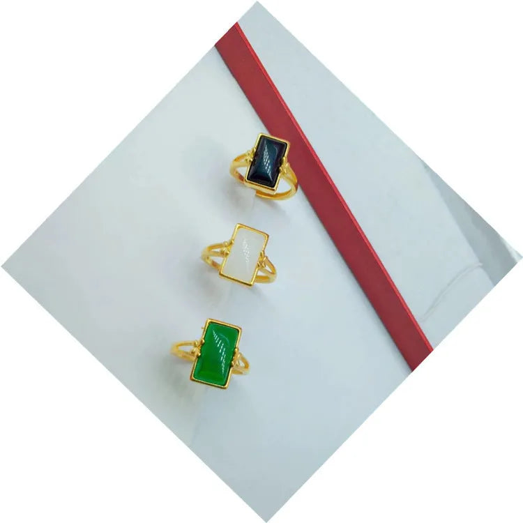 Adjustable gold-coloured brass ring with a large inlaid gemstone, shown in green, white, and black colour options.