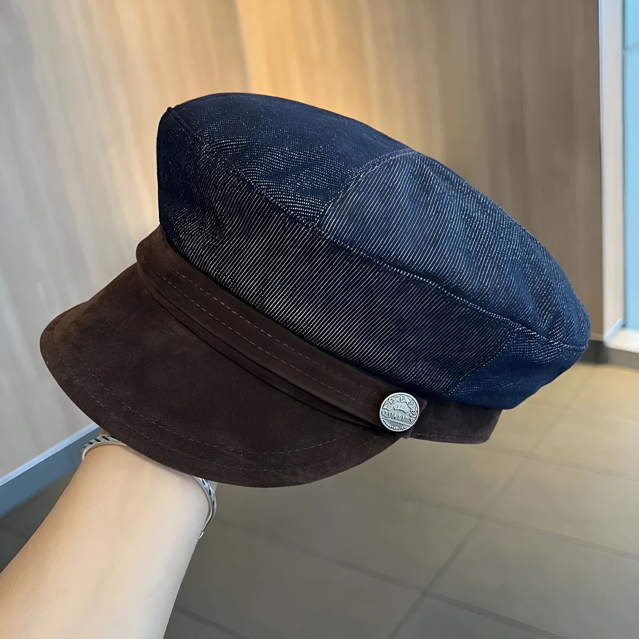 Dark blue denim newsboy cap with an adjustable strap and octagonal shape on a neutral background.