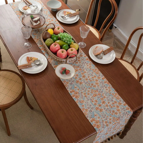 Beige Jacquard table runner with floral pattern and long tassel fringe on a dining table.