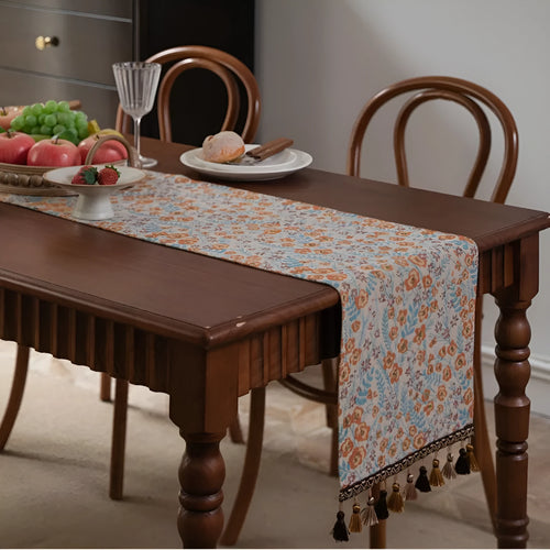 Beige Jacquard table runner with floral pattern and long tassel fringe on a dining table.