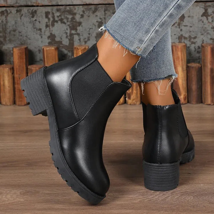Black Chelsea ankle boots for women with flat chunky heel, round toe, and cloth upper on a light background