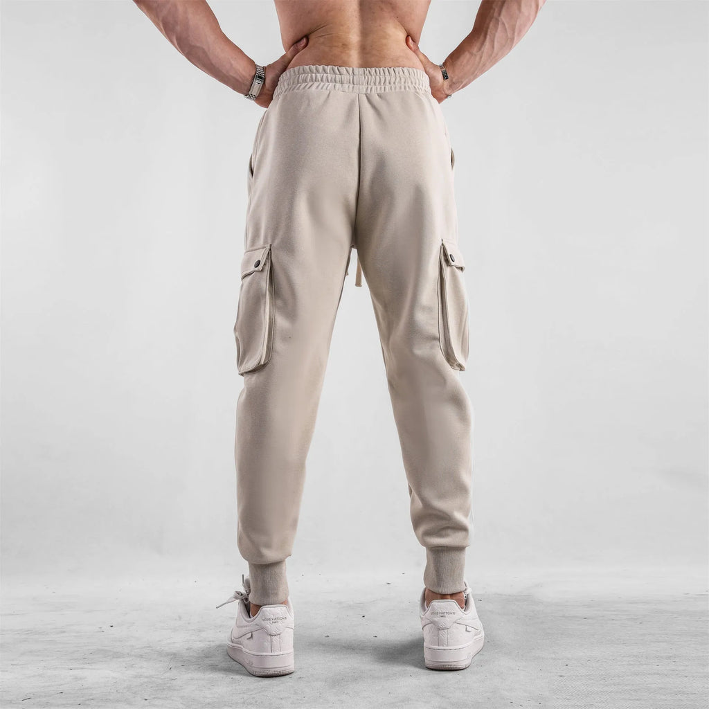 Man wearing loose fit apricot coloured cotton sports trousers with ankle ties and multiple pockets.