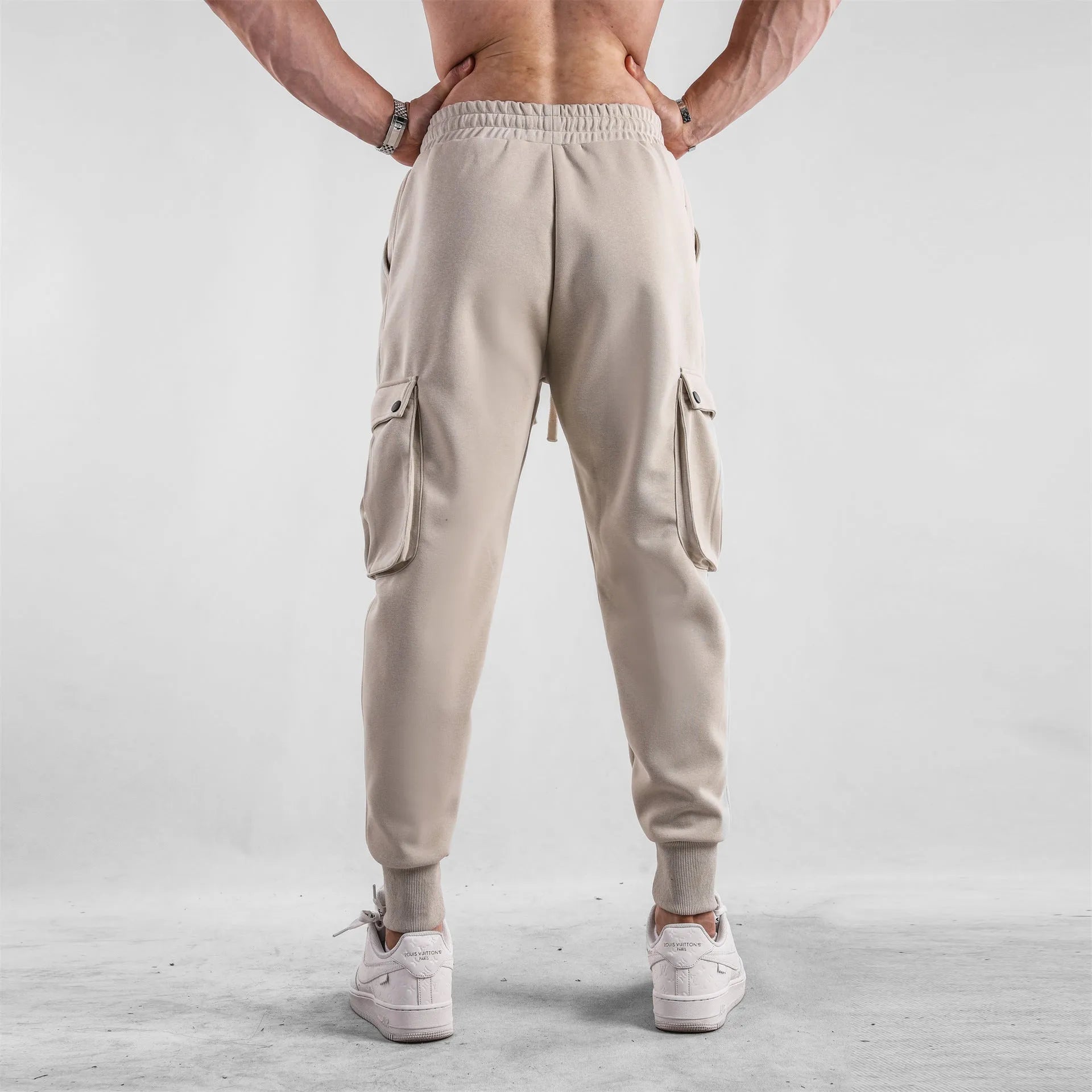 Man wearing loose fit apricot coloured cotton sports trousers with ankle ties and multiple pockets.