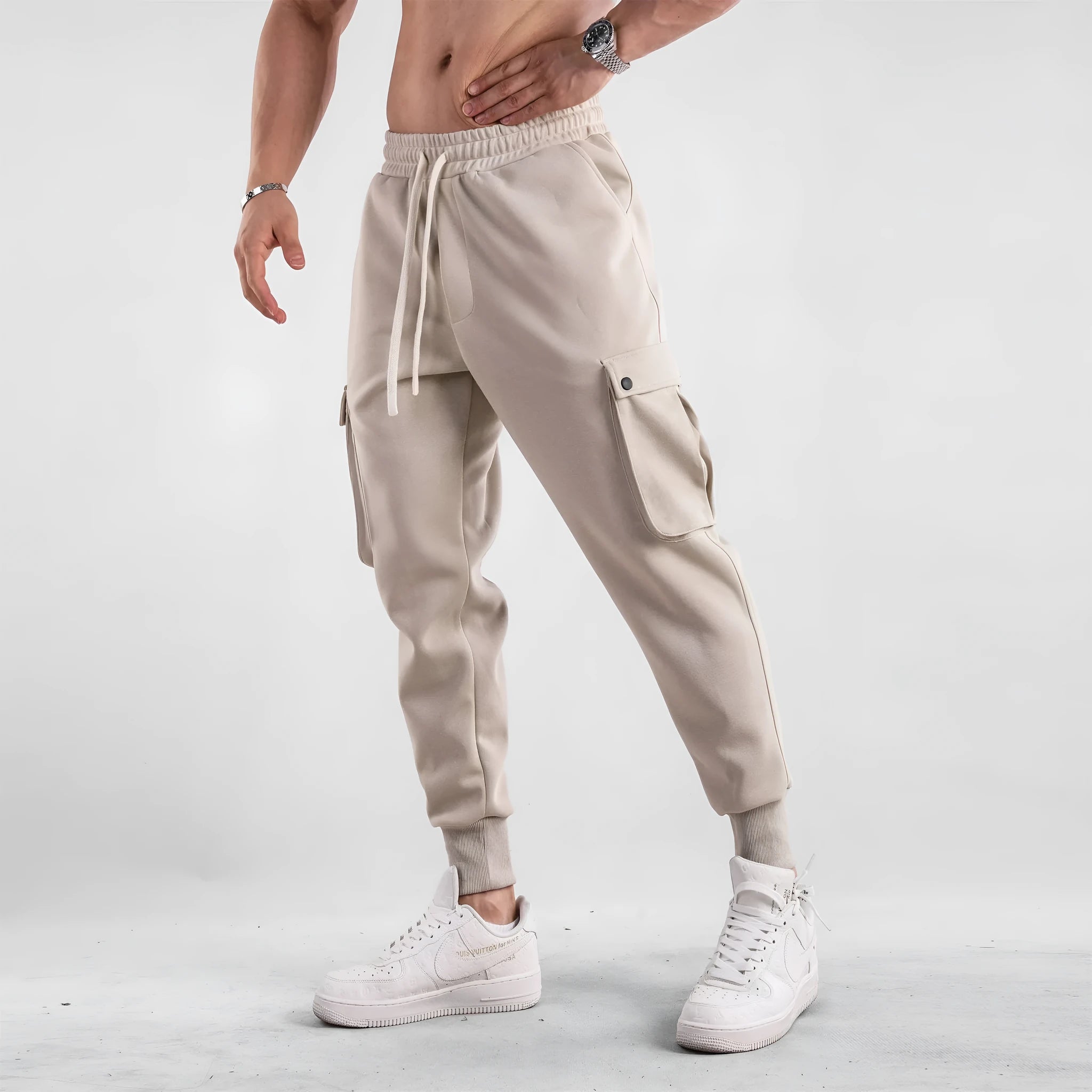 Man wearing loose fit apricot coloured cotton sports trousers with ankle ties and multiple pockets.