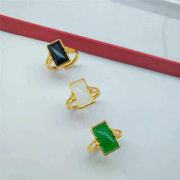 Adjustable gold-coloured brass ring with a large inlaid gemstone, shown in green, white, and black colour options.
