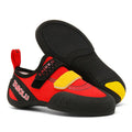 A pair of black and red beginner rock climbing shoes with a Velcro strap and wedge heel on a rocky background.
