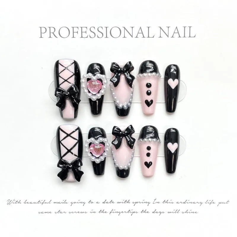 Black plastic false nails with hand-painted pink hearts, bow, and XINGX patterns in cat's eye style.
