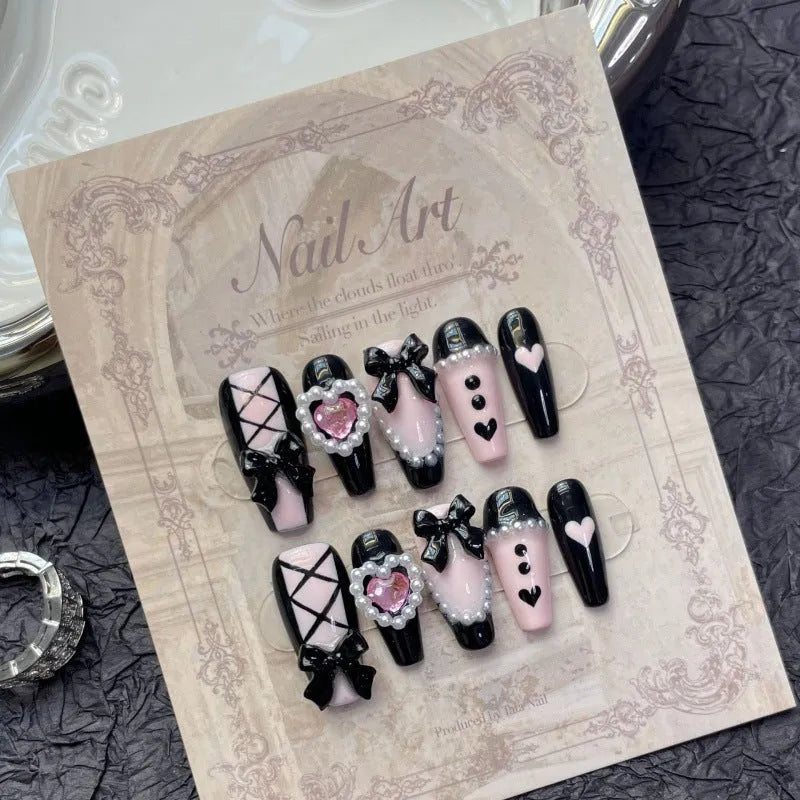 Black plastic false nails with hand-painted pink hearts, bow, and XINGX patterns in cat's eye style.
